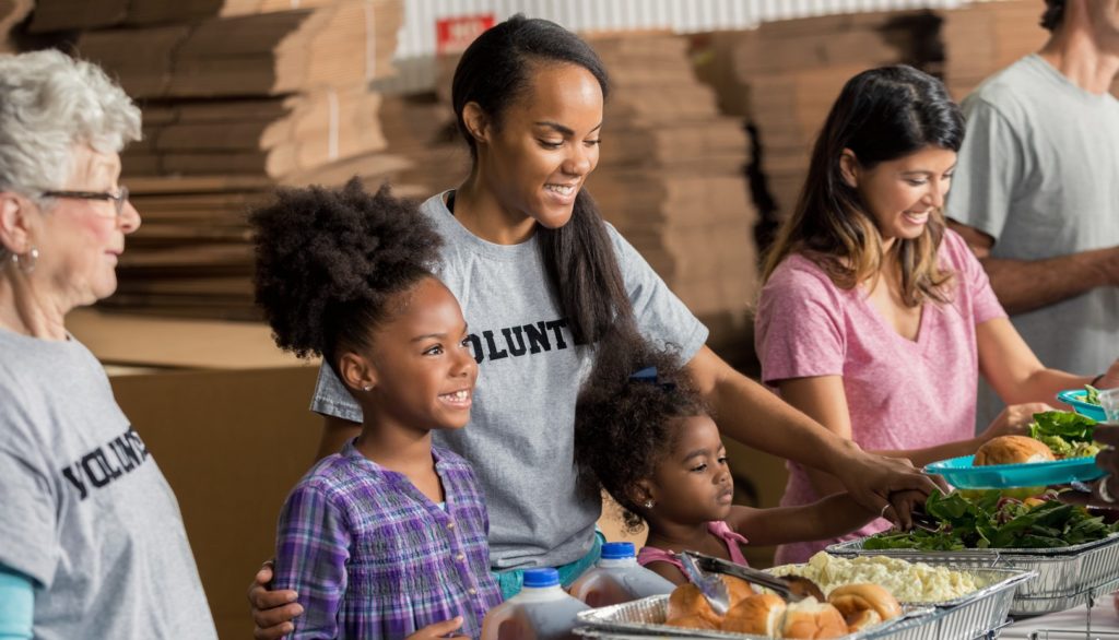 African American mother and her two daughters serve meals to the homeless with their diverse family.